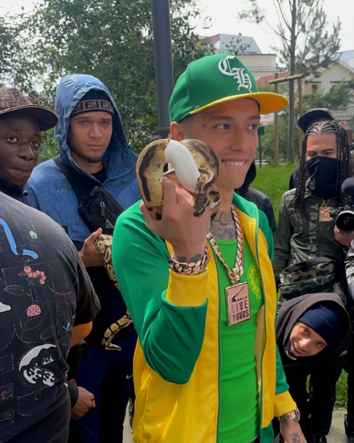 Tournage de clip en extérieur, un homme en casquette verte tient un serpent au milieu d'un groupe
